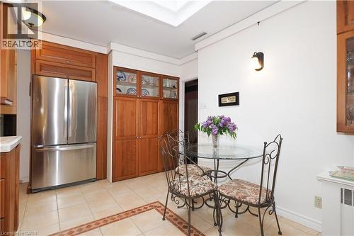 Kitchen featuring a built-in stainless steel refrigerator, extensive wood-finish cabinetry with glass-front display cabinets, light-toned tile flooring, and a ceiling-mounted light fixture - 2023 Coronation Boulevard, Cambridge, ON - Indoor Photo Showing Dining Room