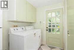 Dedicated laundry area featuring overhead cabinetry, a paneled exterior door with multiple glass lites, and checkerboard floor tiles - 