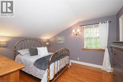 Room featuring sloped ceilings, wood-finish flooring, a double-hung window with blinds, and wall sconce lighting - 