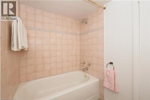 Bathroom featuring a standard bathtub with shower, light-toned square wall tiles, a decorative accent tile band, and polished chrome fixtures - 2023 Coronation Boulevard, Cambridge, ON - Indoor Photo Showing Bathroom