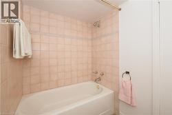 Bathroom featuring a standard bathtub with shower, light-toned square wall tiles, a decorative accent tile band, and polished chrome fixtures - 