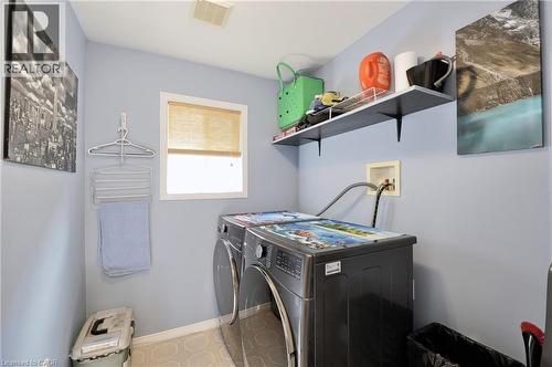 Dedicated laundry area featuring front-loading appliances, a built-in shelf with wall-mounted brackets, and a window with a natural fiber shade - 12 Karalee Crescent, Cambridge, ON - Indoor Photo Showing Laundry Room