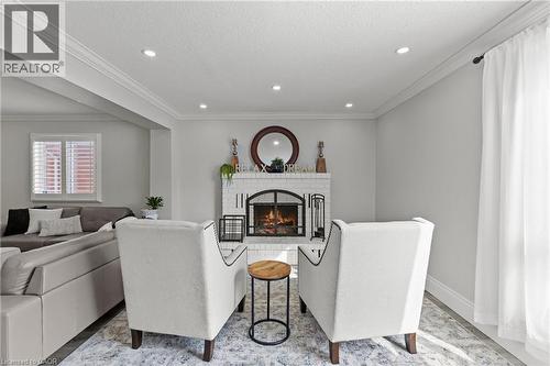 Living area featuring a white brick fireplace with a black arched insert, recessed lighting, crown molding, and a large window with white plantation shutters - 27 Barbara Court, Hamilton, ON - Indoor With Fireplace