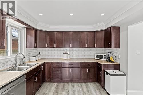 U-shaped kitchen featuring dark wood cabinetry, light-toned countertop, white subway tile backsplash, and stainless steel sink - 27 Barbara Court, Hamilton, ON - Indoor Photo Showing Kitchen With Double Sink