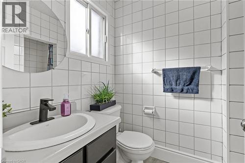 Bathroom featuring white square tile walls, a window with privacy glass, a vanity with an integrated sink, a matte black faucet, and a wall-mounted round mirror - 27 Barbara Court, Hamilton, ON - Indoor Photo Showing Bathroom
