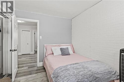Room featuring wood-finish flooring, a white brick-patterned accent wall, and light gray painted walls - 27 Barbara Court, Hamilton, ON - Indoor Photo Showing Bedroom
