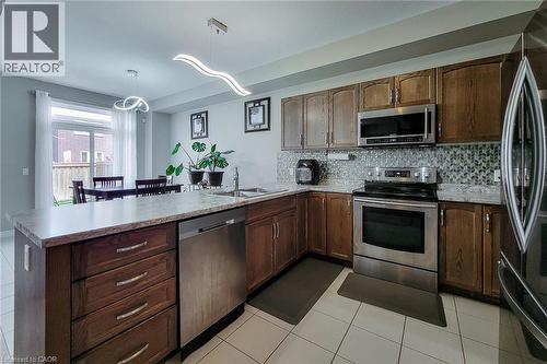 Contemporary kitchen featuring wood-finish cabinetry, stainless steel appliances, light-toned countertops, and a patterned tile backsplash - 40 Fairgrounds Drive, Binbrook, ON - Indoor Photo Showing Kitchen With Stainless Steel Kitchen