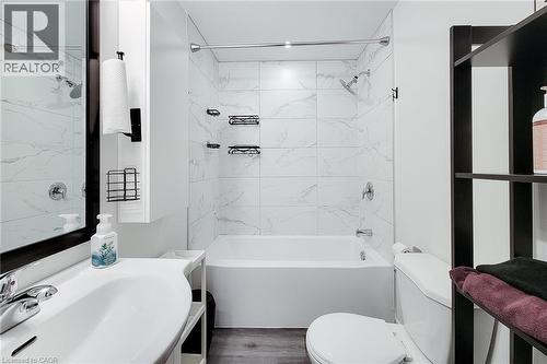 Bathroom featuring a white vanity with a single basin sink, a framed mirror, a built-in bathtub with shower, white tiled walls, and wood-finish flooring - 40 Fairgrounds Drive, Binbrook, ON - Indoor Photo Showing Bathroom