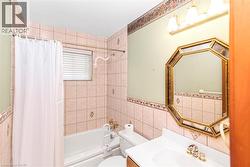 Bathroom featuring a combination tub/shower with tiled surround, a vanity with an integrated sink, an octagonal mirror, and wall-mounted light fixture - 