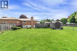 Expansive green lawn featuring a storage shed with double doors, wood fencing, and a chain-link fence - 