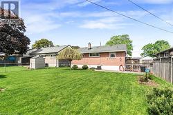 Expansive backyard featuring a manicured lawn, mature trees, a wooden shed, and a privacy fence - 