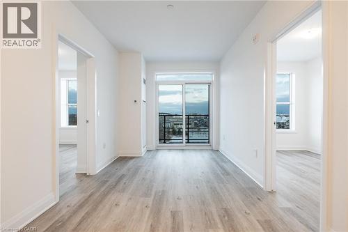 Open-concept living area with light wood-finish flooring, white walls, and a sliding glass door leading to a balcony - 1936 Rymal Road E Unit# 512, Hamilton, ON - Indoor Photo Showing Other Room