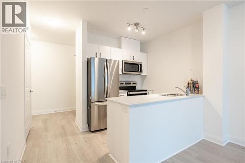 Modern kitchen featuring stainless steel appliances, white cabinetry, a light-toned countertop, a breakfast bar peninsula, and wood-finish flooring - 1936 Rymal Road E Unit# 512, Hamilton, ON - Indoor Photo Showing Kitchen With Stainless Steel Kitchen