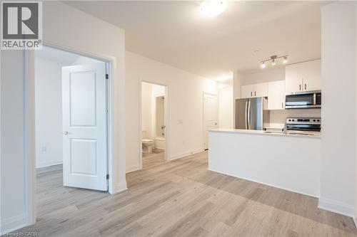 Open-concept living space featuring wood-finish flooring, a contemporary kitchen with stainless steel appliances, white cabinetry, and a peninsula countertop - 1936 Rymal Road E Unit# 512, Hamilton, ON - Indoor Photo Showing Kitchen