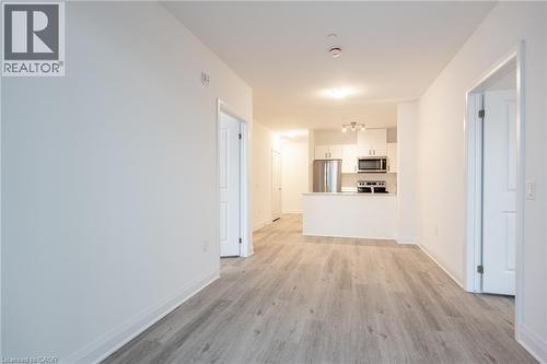 Contemporary interior featuring light wood-finish flooring, white walls, and a kitchen with white cabinetry, stainless steel appliances, and track lighting - 1936 Rymal Road E Unit# 512, Hamilton, ON - Indoor