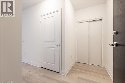 Entryway featuring wood-finish flooring, a white two-panel interior door with brushed nickel hardware, and a closet with sliding panel doors - 1936 Rymal Road E Unit# 512, Hamilton, ON - Indoor Photo Showing Other Room