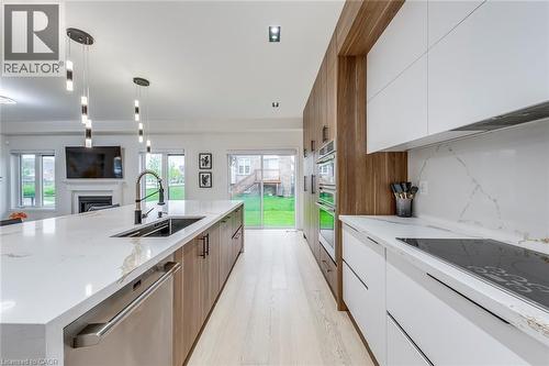 Contemporary kitchen featuring a large center island with integrated sink, sleek white and wood-finish cabinetry, built-in stainless steel appliances, and light wood-finish flooring - 3937 Leonardo Street, Burlington, ON - Indoor Photo Showing Kitchen