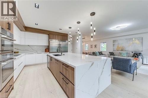 Open-concept kitchen featuring an expansive island with a waterfall countertop, integrated stainless steel appliances, wood-finish and white cabinetry, recessed lighting, and wood-finish flooring - 3937 Leonardo Street, Burlington, ON - Indoor Photo Showing Kitchen With Upgraded Kitchen