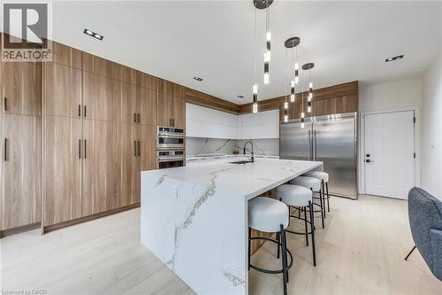 Gourmet kitchen featuring a waterfall island with a quartz countertop, integrated sink with a matte black faucet, full-height wood-finish cabinetry, and stainless steel built-in appliances - 3937 Leonardo Street, Burlington, ON - Indoor Photo Showing Kitchen With Upgraded Kitchen