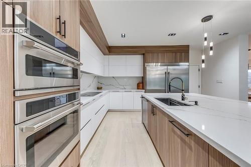 Modern kitchen featuring light wood-finish and white cabinetry, integrated stainless steel appliances, a large center island with an undermount sink, and light-toned flooring - 3937 Leonardo Street, Burlington, ON - Indoor Photo Showing Kitchen With Upgraded Kitchen