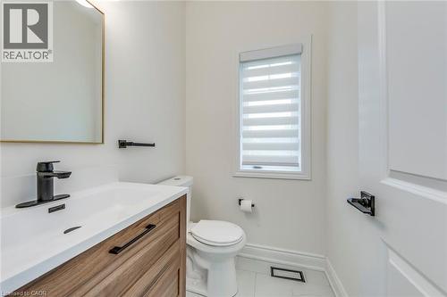 Bathroom featuring a wood-finish vanity with a white countertop and integrated sink, matte black hardware, a toilet, a window with horizontal blinds, and tile flooring - 3937 Leonardo Street, Burlington, ON - Indoor Photo Showing Bathroom