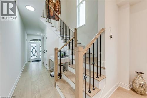 Foyer featuring a grand staircase with light wood railings and wrought iron balusters, light wood-finish flooring, and white walls - 3937 Leonardo Street, Burlington, ON - Indoor Photo Showing Other Room