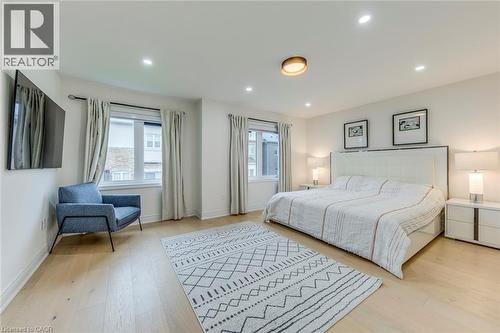 Spacious bedroom featuring light wood-finish flooring, recessed lighting, and dual windows with curtains - 3937 Leonardo Street, Burlington, ON - Indoor Photo Showing Bedroom