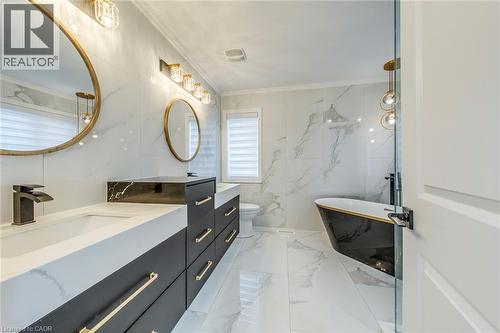 Contemporary bathroom featuring a freestanding black and gold bathtub, dual vanity with undermount sinks, gold-accented hardware, rectangular mirrors, and large format white marble-look tile flooring - 3937 Leonardo Street, Burlington, ON - Indoor Photo Showing Bathroom