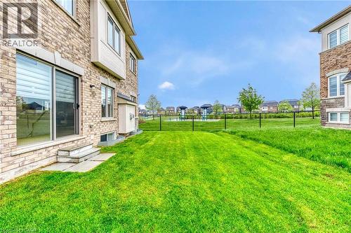 Rear exterior featuring a brick facade, sliding glass patio door, stone steps, a manicured lawn, and a black metal fence - 3937 Leonardo Street, Burlington, ON - Outdoor