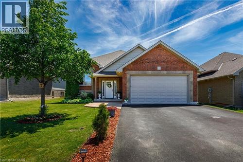 Traditional-style home featuring a brick facade, attached two-car garage, asphalt driveway, mature front yard tree, and a paved walkway leading to the front entry - 10 Redbud Crescent, Simcoe, ON - Outdoor