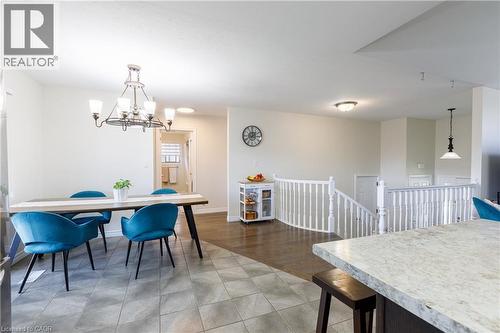 Open-concept living area featuring a tile-floored dining space with a chandelier, wood-finish flooring, a white staircase with balusters, and a light-colored kitchen countertop - 10 Redbud Crescent, Simcoe, ON - Indoor Photo Showing Dining Room