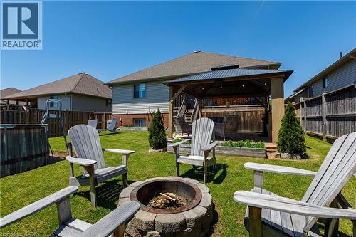 Expansive backyard featuring a built-in fire pit, manicured lawn, and a covered patio structure with string lighting - 10 Redbud Crescent, Simcoe, ON - Outdoor With Deck Patio Veranda