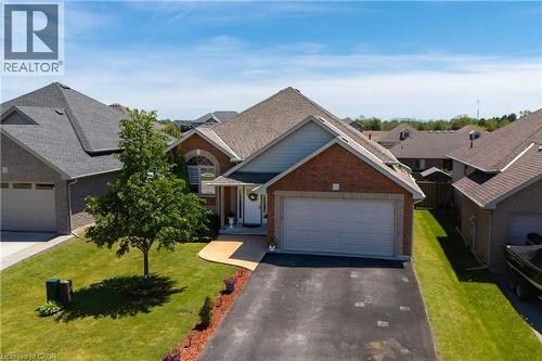 Brick and siding exterior featuring an arched window, attached garage, paved driveway, and manicured lawn - 10 Redbud Crescent, Simcoe, ON - Outdoor With Facade
