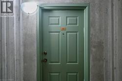 Green panel door with brass-finish hardware set within a textured concrete wall, featuring an overhead wall-mounted light fixture - 