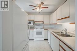 Kitchen featuring white cabinetry with wood-finish trim, white appliances including a built-in microwave, dual basin stainless steel sink, and a ceiling fan with integrated lighting - 