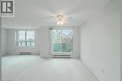 Expansive living space featuring a sliding glass door to a balcony, a large window, wall-to-wall carpeting, a ceiling fan with light fixture, and baseboard heaters - 
