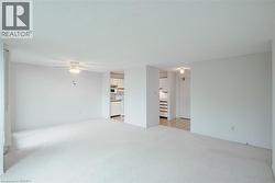 Spacious living area featuring light-colored carpeting, a ceiling fan with integrated lighting, and neutral wall tones - 
