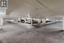 Underground parking garage featuring concrete flooring, concrete support columns, overhead lighting, and numbered parking spaces - 
