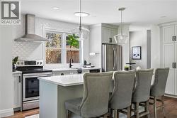 Modern kitchen featuring a central island with countertop seating, stainless steel appliances, a range hood, and light-toned cabinetry - 