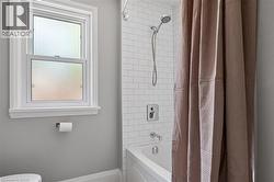 Bathroom featuring a full tub with shower, subway tile surround, and a frosted privacy window - 