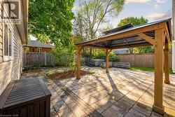 Expansive backyard featuring a stone paver patio, a wooden gazebo with a dark metal roof, a built-in stone planter, a hot tub, and a privacy fence - 