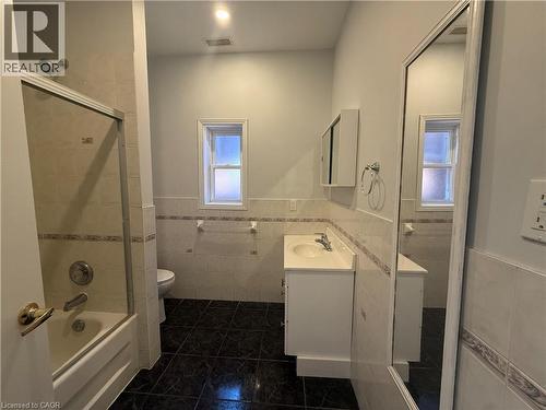 Bathroom featuring a shower/tub combination with sliding glass doors, white vanity with integrated sink, wall-mounted medicine cabinet, and dark tile flooring - 359 Barton Street E Unit# Upper, Hamilton, ON - Indoor Photo Showing Bathroom