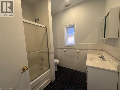 Bathroom featuring a shower/tub combination with sliding frosted glass doors, a single window, a wall-mounted medicine cabinet, and a vanity with an integrated sink and chrome faucet - 359 Barton Street E Unit# Upper, Hamilton, ON - Indoor Photo Showing Bathroom