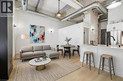 Open-concept living space featuring high ceilings with exposed ductwork, light wood-finish flooring, and white walls - 