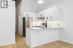 Modern kitchen featuring white shaker cabinetry, stainless steel appliances, a white tile backsplash, and wood-finish flooring - 