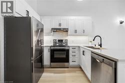 Modern kitchen featuring white cabinetry, stainless steel appliances, a black matte faucet, light-toned countertops, and wood-finish flooring - 