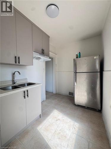 Kitchen featuring gray cabinetry with matte black hardware, a double basin stainless steel sink, a stainless steel refrigerator, and tiled flooring - 10 Fairleigh Avenue N, Hamilton, ON - Indoor Photo Showing Kitchen With Double Sink