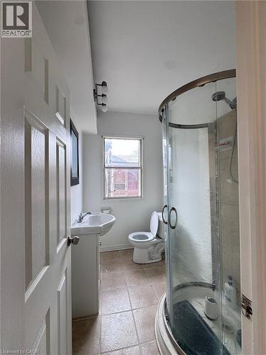 Bathroom featuring a curved glass shower enclosure, square floor tiles, pedestal sink, and a window providing natural light - 10 Fairleigh Avenue N, Hamilton, ON - Indoor Photo Showing Other Room