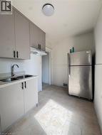 Kitchen featuring gray cabinetry with matte black hardware, a double basin stainless steel sink, a stainless steel refrigerator, and tiled flooring - 