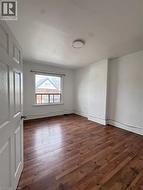 Room featuring wood-finish flooring, white painted walls, a window with exterior residential structures visible, a white paneled door, and a flush-mount ceiling light fixture - 